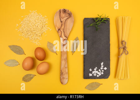 Gli ingredienti della cucina luminosa su sfondo giallo. Uova, spaghetti, pasta orzo, foglie di alloro. Foto Stock