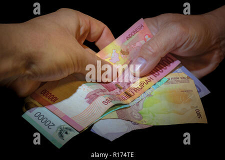 Due mani, uno indonesiani e uno di bianco caucasico consegnare banconote indonesiano all'altra. Concetto di affare. Foto Stock