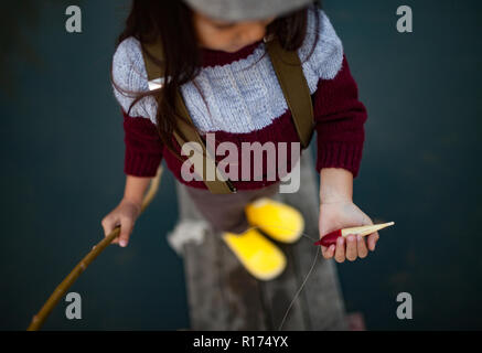 Bambino ragazza si alza e tiene nelle sue mani self-made canna da pesca e flottazione. Primo piano. Vista dall'alto. Foto Stock