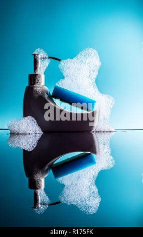 Piccolo bagno con una spugna e schiuma con la riflessione su uno sfondo blu, detergente Foto Stock