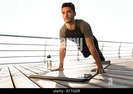 Foto di giovani bello uomo di sport all'aperto sulla spiaggia fare sport esercizi vicino a bottiglia con acqua. Foto Stock