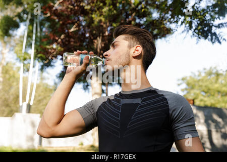 Immagine dei giovani concentrato uomo di sport all'aperto nel parco alla ricerca da parte di acqua potabile. Foto Stock