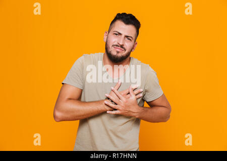 Ritratto di un giovane uomo informale in piedi isolato su sfondo arancione, avente un attacco di cuore Foto Stock