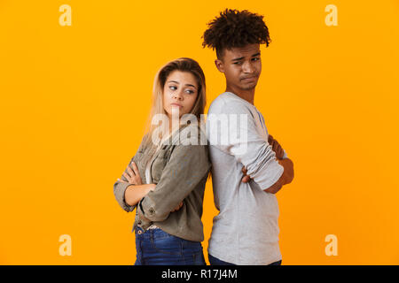 Ritratto di un deluso multietnica giovane in piedi isolato su sfondo giallo, dorso a dorso Foto Stock