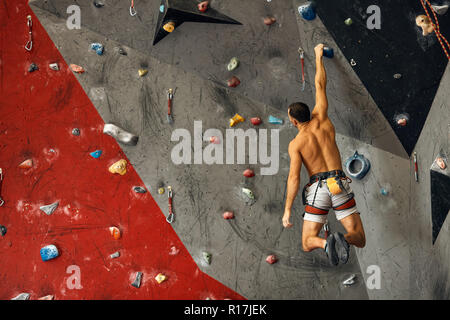 Panoramica del giovane uomo muscolare in allenamento indoor clymbing palestra. Foto Stock