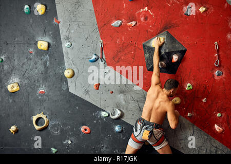 Panoramica del giovane uomo muscolare in allenamento indoor clymbing palestra. Foto Stock