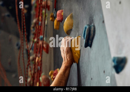 Macro shot degli scalatori delle mani di presa delle maniglie colorate durante l'allenamento indoor Foto Stock