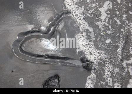 Un cuore lucido verniciato in spiaggia sabbiosa semi lavati via dalle onde Foto Stock