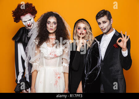 Gruppo di amici vestito in costumi spaventosi celebrare Halloween isolate su sfondo giallo Foto Stock