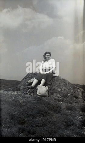 Degli anni Cinquanta, storico, una piccola tor o craig, exmoor, Inghilterra, Regno Unito. una signora seduta walker, appoggiato sulla roccia con il suo bastone da passeggio e sacchetto per terra accanto a lei. Foto Stock