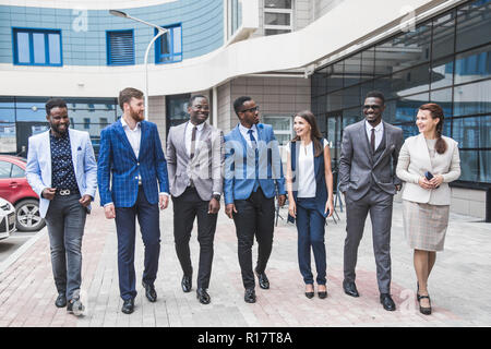 Il successo della società con lavoratori felice. Le donne e gli uomini in abiti aziendali stand con le braccia incrociate contro lo sfondo dei grattacieli. Foto Stock