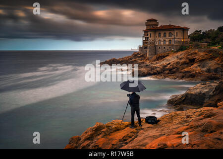 Fotografo con ombrellone al Boccale Castello sulla costa rocciosa vicino a Livorno, Italia Foto Stock