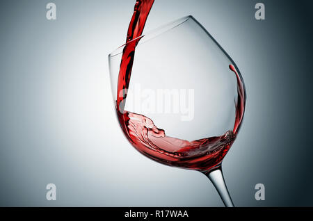 Versare il vino rosso in vetro inclinato e sfondo grigio Foto Stock