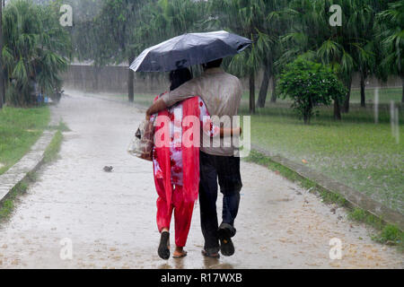 Una giovane coppia a piedi sotto la pioggia con un ombrello. Dacca in Bangladesh. Foto Stock