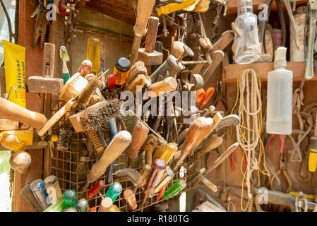 Più utensili a mano, spray e altri contenitori lungo con pezzi di spago e corda appesa da ripiani in un cortile officina Foto Stock