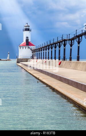 Alla fine del suo molo con passerella sopraelevata, il faro di Michigan City, Indiana è illuminata da un albero di luce del sole mentre Dark nuvole temporalesche a Foto Stock