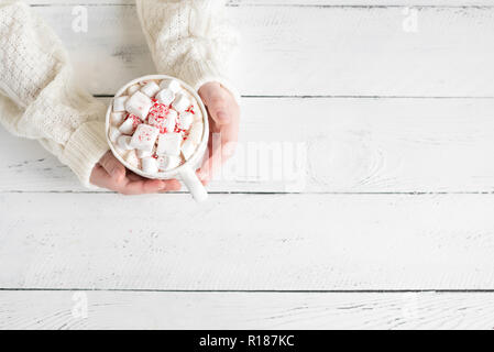 Il Natale di cioccolata calda con marshmallows, menta piperita caramelle in mani sul tavolo bianco, vista dall'alto, copia dello spazio. Foto Stock