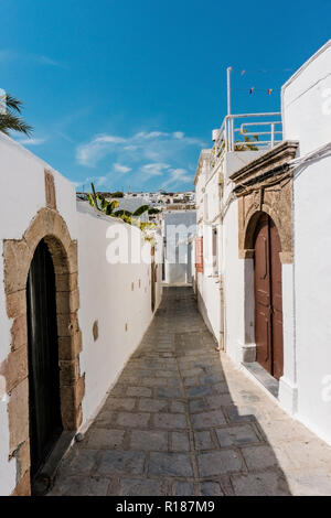 Foto verticale con vuoto street. Street ha case bianche su entrambi i lati tipiche di questa città Lindos sull' isola di Rodi. La superficie di strada è realizzato da squ Foto Stock