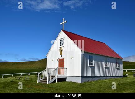 Una piccola chiesa bianca in Islanda con un tetto rosso. Giornate di sole e un cielo blu. Foto Stock