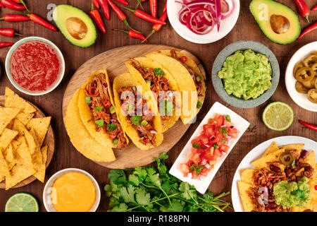 Una foto del cibo messicano, compresi i tacos, guacamole, Pico de Gallo, nachos e altri, girato dalla parte superiore con ingredienti al buio su un legno rustico indietro Foto Stock