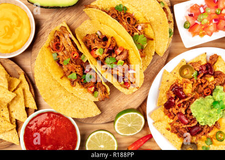 Una foto del cibo messicano, compresi i tacos, guacamole, Pico de Gallo e nachos con chili con carne, girato dalla parte superiore con ingredienti su uno sfondo di legno Foto Stock