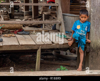 Thakhek, Laos - 21 Aprile 2018: a piedi nudi bambino seduto di fronte a una casa in un remoto villaggio rurale nella provincia Khammouane in Laos Foto Stock