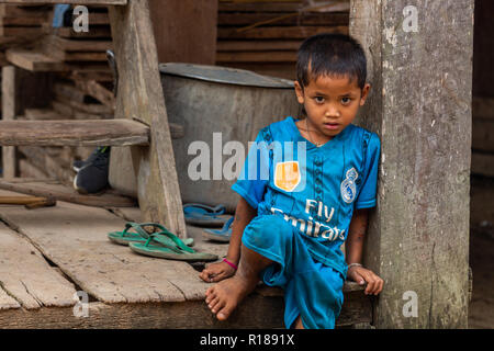 Thakhek, Laos - 21 Aprile 2018: a piedi nudi bambino seduto di fronte a una casa in un remoto villaggio rurale nella provincia Khammouane in Laos Foto Stock