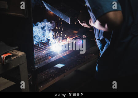 Thai studente di ingegneria elettrica eseguire la saldatura dei metalli sul banco di lavoro in classe officina con un sacco di scintille Foto Stock