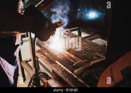 Thai studente di ingegneria elettrica eseguire la saldatura dei metalli sul banco di lavoro in classe officina con un sacco di scintille Foto Stock