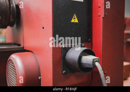 Tensione alta adesivo di avvertenza sul retro di un utensile elettrico in officina Foto Stock