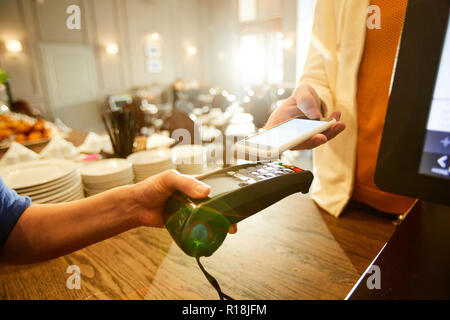 Client del moderno Cafe' tenendo il suo smartphone sulla macchina di pagamento trattenuto da parte del personale Foto Stock