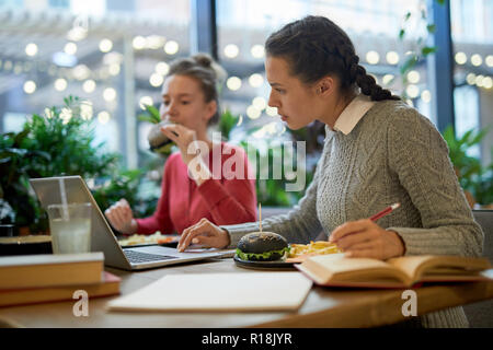 Una delle ragazze ricerca nella rete durante la preparazione di assegnazione iniziale durante il pranzo in un college cafe Foto Stock