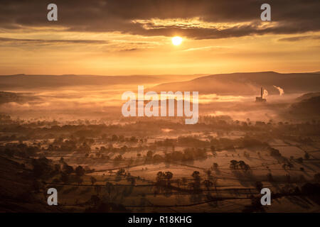 Bright sole splendere la luce dorata su una nebbiosa valle del Peak District, Inghilterra, Regno Unito. Alberi cast forti ombre attraverso i campi in primo piano. Foto Stock