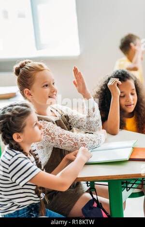 Felice studentesse seduti in classe durante la lezione e alzando le mani Foto Stock