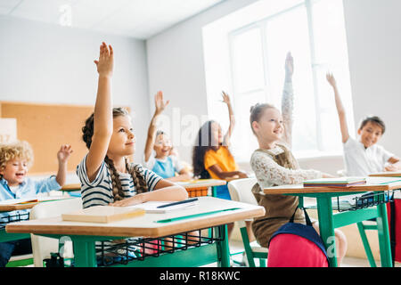 Un gruppo di scolari alzando le mani per rispondere alla domanda durante la lezione Foto Stock