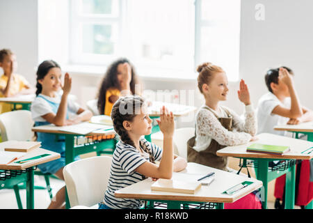 Un gruppo di compagni di classe alzando le mani per rispondere alla domanda durante la lezione Foto Stock