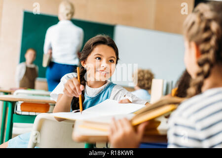 Happy Little Schoolgirl parlando con un compagno di classe durante la lezione Foto Stock