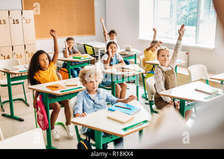 Un gruppo di alunni alzando le mani per rispondere alla domanda durante la lezione in aula Foto Stock