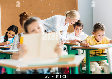 Maestro sorridente aiutando i bambini con il lavoro durante la lezione Foto Stock