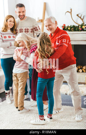 Felice che abbraccia i nonni con i bambini durante la vigilia di Natale a casa Foto Stock