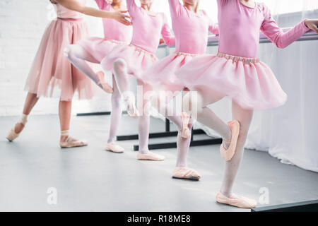 Ritagliato colpo di bambini in rosa tutu gonne pratica di balletto con insegnante nella scuola di danza Foto Stock