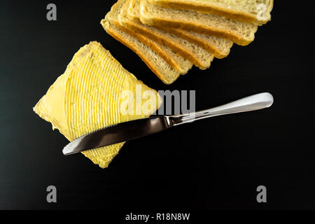 Il burro con belle macchie e un coltello su un pezzo di pane di close-up su sfondo scuro Foto Stock