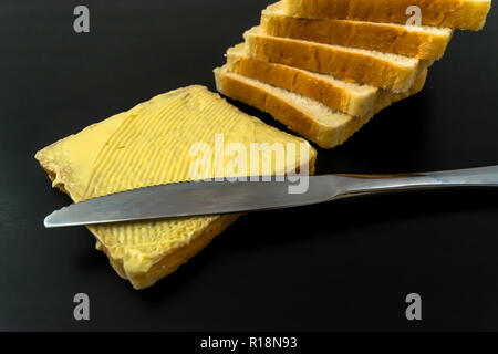 Il burro con belle macchie e un coltello su un pezzo di pane di close-up su sfondo scuro Foto Stock