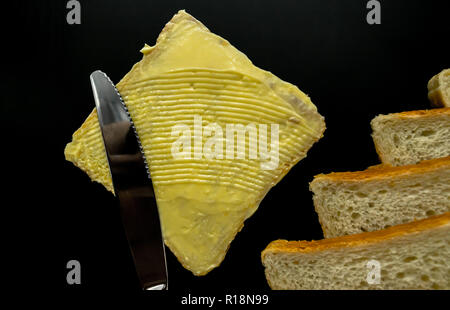 Il burro con belle macchie e un coltello su un pezzo di pane di close-up su sfondo scuro Foto Stock