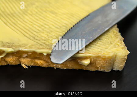 Il burro con belle macchie e un coltello su un pezzo di pane di close-up su sfondo scuro Foto Stock