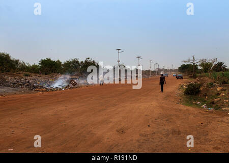 Bissau, Repubblica di Guinea Bissau - 5 Febbraio 2018: la gente camminare lungo una strada sterrata circondata da una discarica nella periferia della città di Bissau Foto Stock