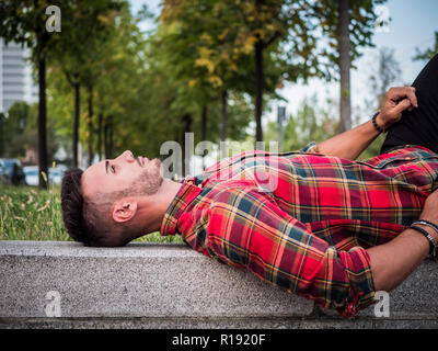 Un bel giovane uomo nel contesto urbano in città europea moderna, i jeans e rosso camicia a scacchi Foto Stock