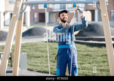 Bello operaio in uniforme swing di montaggio sul parco giochi all'aperto Foto Stock