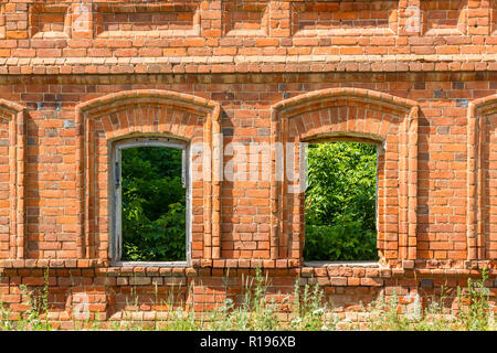 Due finestre del vecchio distrutto edificio di mattoni rossi attraverso la quale è possibile vedere le piante verdi ed erba. Foto Stock