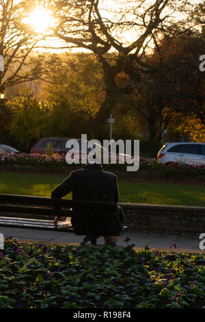 L'uomo si sedette su un sedile mentre il sole comincia a tramontare in un tardo pomeriggio d'autunno ad Harrogate, nel Nord Yorkshire, Inghilterra, Regno Unito. Foto Stock
